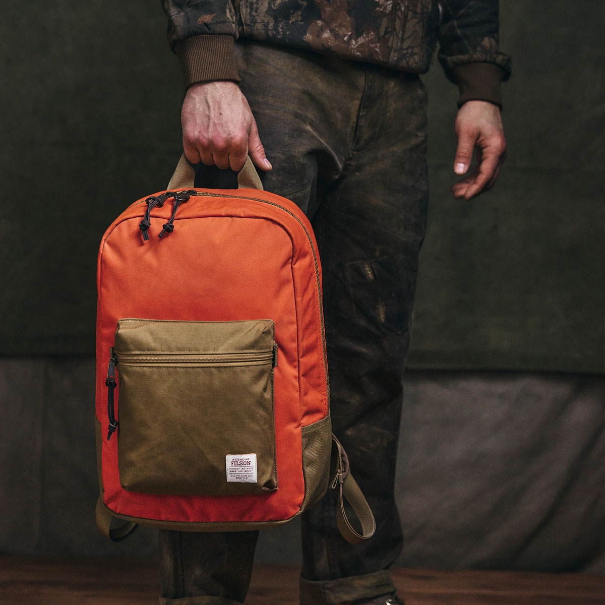 Filson Surveyor 25L Backpack Dark Tan/Flame, am Handgriff getragen